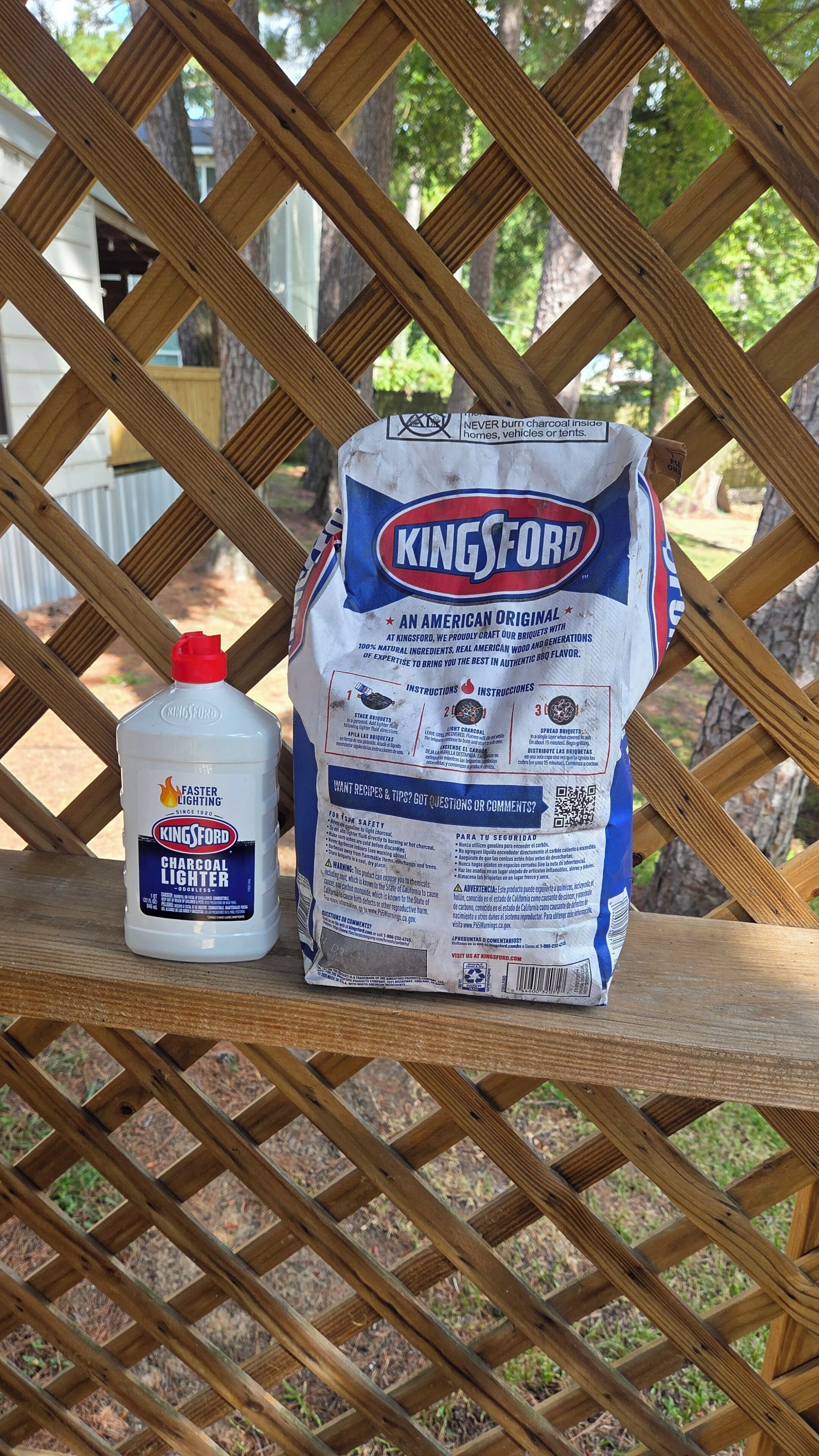 A bag of Kingsford charcoal briquettes and a bottle of Kingsford Charcoal Lighter on a wooden lattice structure.