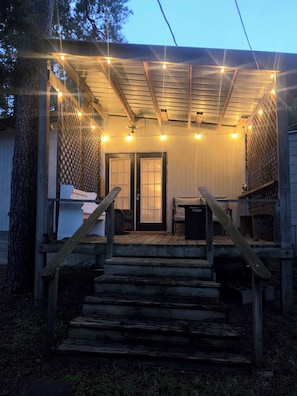 A wooden deck with a covered seating area, a staircase leading up, and string lights.