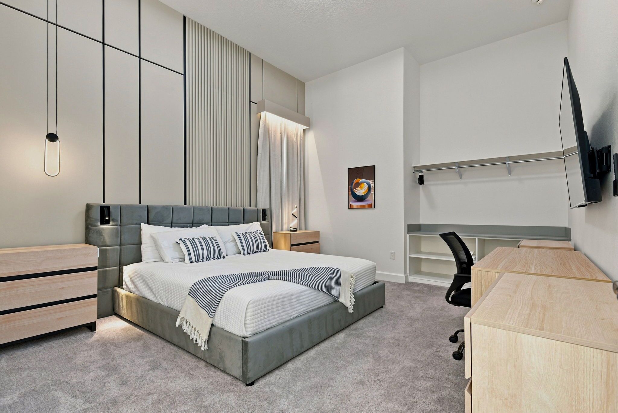 Une chambre à coucher moderne, équipée d’un lit, de tables de chevet, d’un bureau et d’un téléviseur fixé au mur.