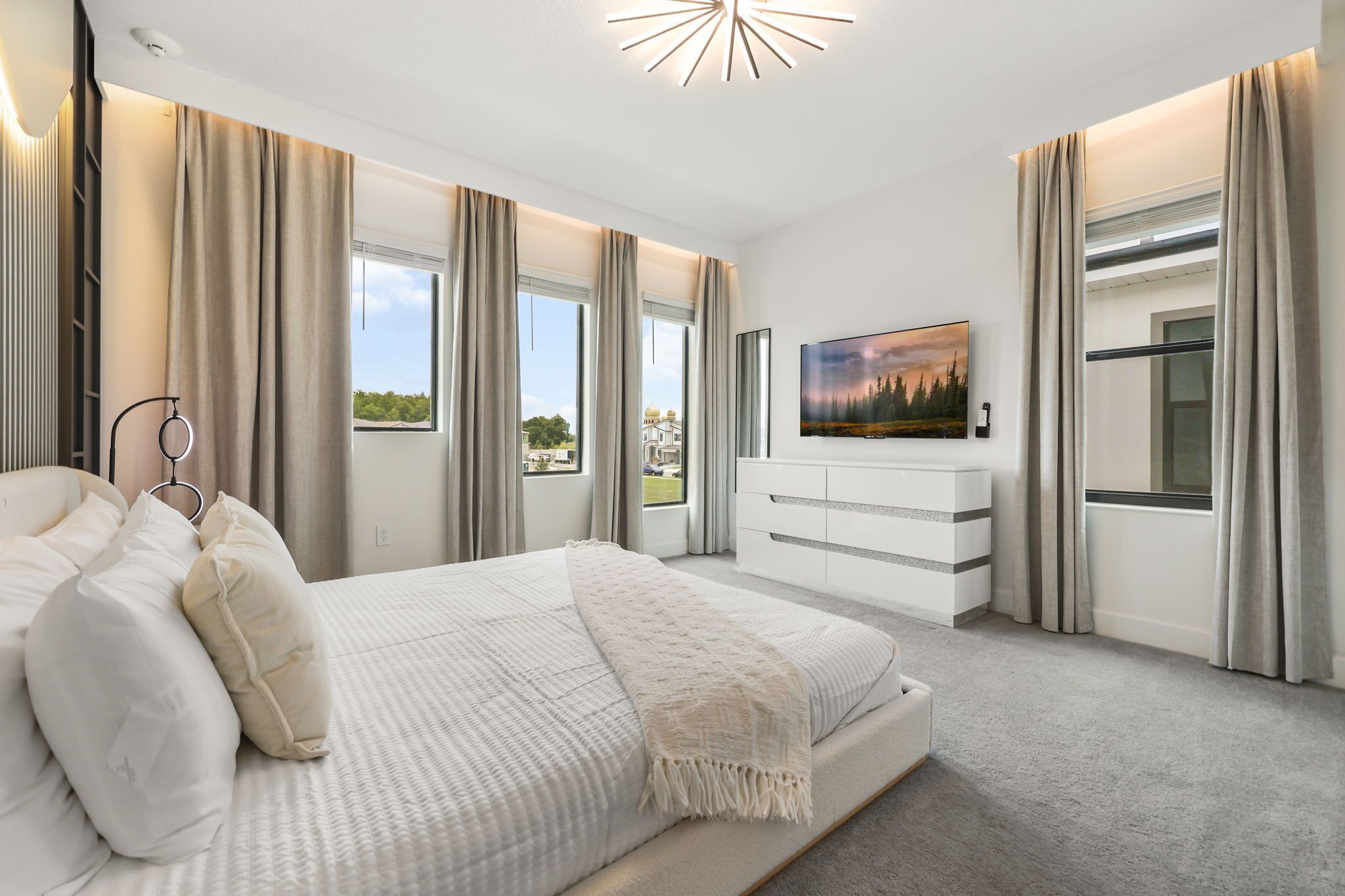 A modern bedroom with a large bed, a TV, and a view of the outdoors.
