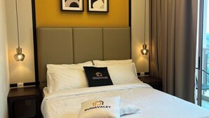 Habitació d'hotel amb llit, dos almoinos, una taula de nit, llum penjada a la paret i una finestra amb cortines.