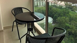 Un balcó amb taula i dues cadires, amb vista a un paisatge urbà ple d'edificis alts i zones verdes.