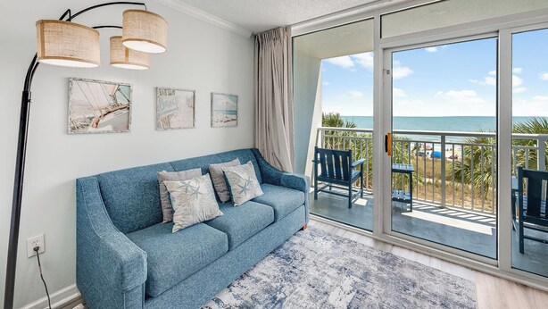 A blue sofa with cushions, a floor lamp, and artwork on a wall. - Direct Oceanfront  Amazing Views In Camelot Resort (Myrtle Beach)