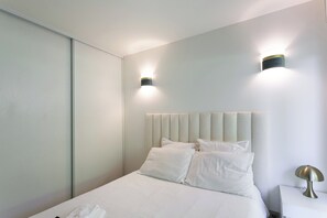 A modern hotel room with a large bed, two wall-mounted lights, and a bedside table with a lamp. - Apartment with pool (Nice)