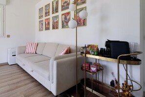 A living room with a sofa, a coffee table, a floor lamp, a bookshelf, and a wall with framed pictures. - Apartment with pool (Nice)