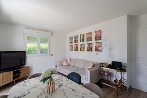 A modern living room with a sofa, TV, and a dining table with a vase. - Apartment with pool (Nice)