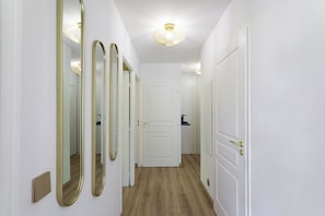 A hallway with white walls, a wooden floor, and three mirrors. There is a white door at the end of the hallway. - Apartment with pool (Nice)