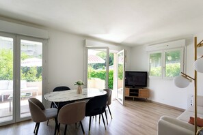 A modern living room with a dining area, large windows, and a television. - Apartment with pool (Nice)