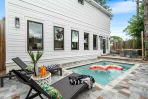 A pool area with lounge chairs, a small table, and a wooden fence. - Coastal Retreat - Private Pool - Easy Beach Access (Panama City Beach)