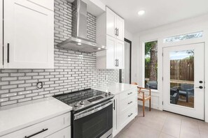 A kitchen with white cabinets, a brick backsplash, a stainless steel range hood, and a sliding glass door leading to an outdoor area. - Coastal Retreat - Private Pool - Easy Beach Access (Panama City Beach)