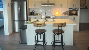 Eine moderne Küche mit Edelstahlgeräten, Holzbarhocker und hellen Schränken.