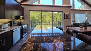 A modern kitchen with dark cabinetry, a marble countertop, and a large sliding glass door leading to a balcony with a forest view. - Colorado Mountain Retreat - A peaceful Lake View Cabin with Amazing Views! (Idaho Springs)