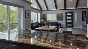 A modern kitchen with a granite countertop, dining area with a wooden table and chairs, and a living room with a black leather sofa. - Colorado Mountain Retreat - A peaceful Lake View Cabin with Amazing Views! (Idaho Springs)