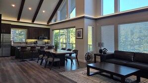 A modern kitchen with dark wood cabinets, a central island, and a dining area with a large window. - Colorado Mountain Retreat - A peaceful Lake View Cabin with Amazing Views! (Idaho Springs)