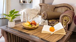 Ein gemütliches Wohnzimmer mit einem gestreiften Sofa, einem kleinen Tisch mit einer Obstschale, einer Topfpflanze und einem Bücherregal.
