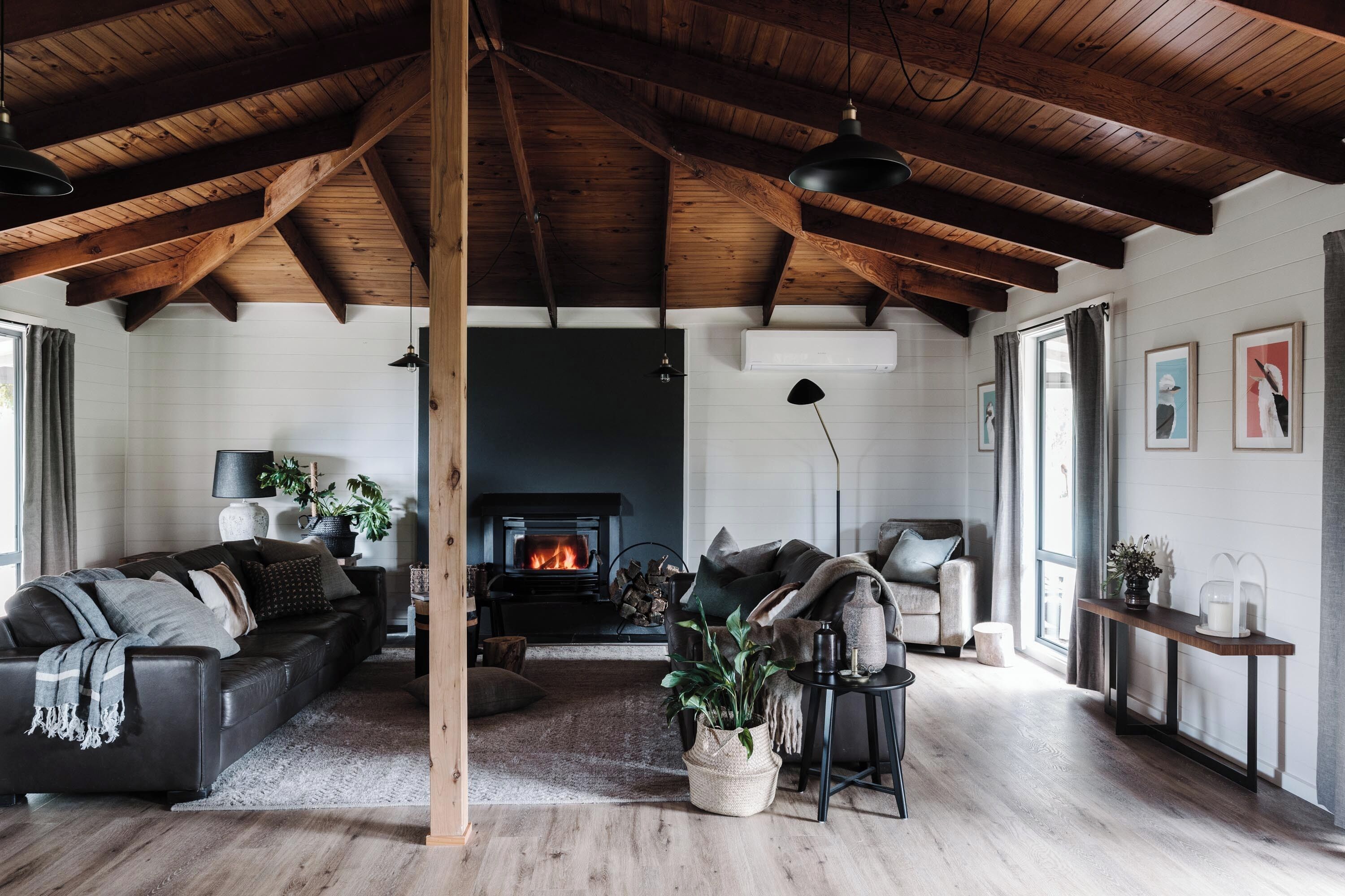 A cozy living room with a fireplace, wooden beams, and a sofa set.