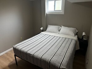 Ein Schlafzimmer mit einem Bett, zwei Nachttischlampen, einem Fenster und einer Tür.