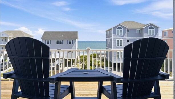 Zwei Adirondack-Stühle auf einer Holzterrasse mit Blick auf Häuser und das Meer.