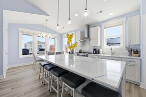 A modern kitchen with a large island, white cabinetry, and pendant lighting. - Blue Dolphin: Oceanview, game room and Grill (North Topsail Beach)