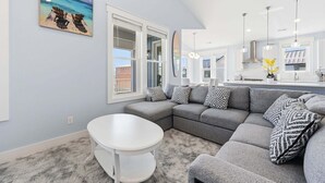 Ein modernes Wohnzimmer mit einem grauen Ecksofa, einem runden weißen Tisch und einem Gemälde von Stühlen am Strand.