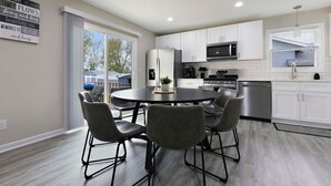 Une cuisine moderne avec des meubles blancs, des appareils en acier inoxydable et une table de salle à manger ronde, assortie de chaises.