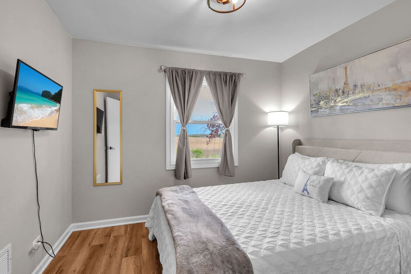 A bedroom with a bed, a TV, a painting, and a window with curtains.