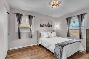 Ein Schlafzimmer mit Bett, Vorhängen, einem Stadtbildgemälde, einer Stehlampe und Blick ins Freie.
