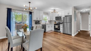 A modern kitchen with white cabinets, stainless steel appliances, and a dining area with a glass table and chairs. - Modern 4BD Home in Lake Hills Pet friendly (Lake in the Hills)