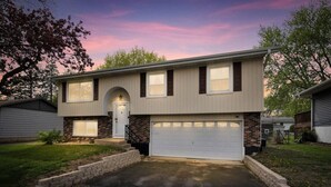 A two-story house with a garage, a front entrance with a door, and a small front yard. - Modern 4BD Home in Lake Hills Pet friendly (Lake in the Hills)