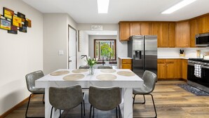 Une cuisine moderne avec des meubles en bois, des appareils en acier inoxydable et un coin repas comprenant une table blanche et des chaises grises.