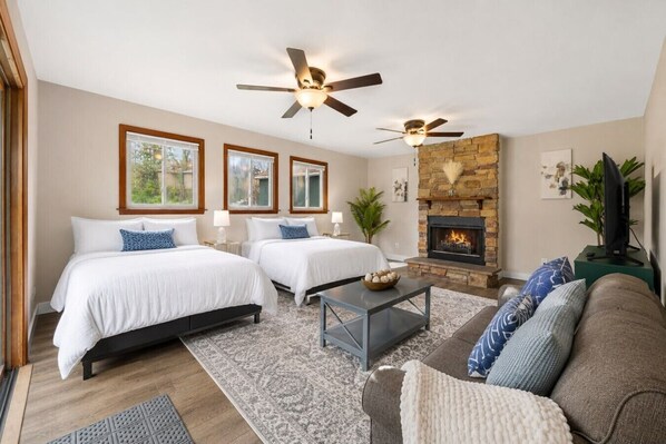 A modern bedroom with two beds, a fireplace, and a ceiling fan.