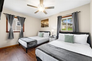 A bedroom with two beds, a ceiling fan, a nightstand, and a window with curtains. - Displaced Housing | 5BR | Pet Friendly (Streamwood)