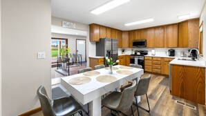 Une cuisine moderne avec des meubles en bois, des appareils en acier inoxydable et un coin repas comprenant une table et des chaises blanches.