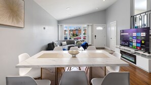 Een moderne woonkamer met een eethoek, een grijze bank, een flatscreen televisie en een groot raam.