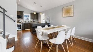 Een moderne keuken met donkere kastjes, een centraal eiland en een eethoek met een witte tafel en stoelen.