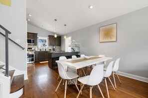 A modern kitchen with dark cabinets, a central island, and a dining area with a white table and chairs. - O’Hare 7-Bed Home | Workers & Insurance (Des Plaines)