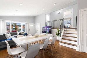 A modern living room with a dining area, a staircase, and a view of the outside. - O’Hare 7-Bed Home | Workers & Insurance (Des Plaines)