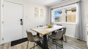 Een eetgedeelte met een tafel, stoelen, een raam met gordijnen en kunst aan de muur.
