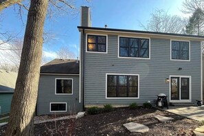 Une maison à deux étages, à l’extérieur gris, dotée de nombreuses fenêtres et d’une cheminée.