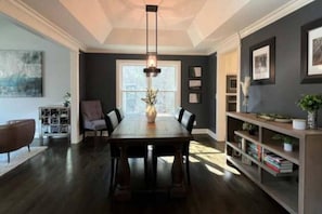 A dining area with a dark wood table, chairs, a pendant light, a bookshelf, and a window with natural light. - Luxury Executive Retreat | Gym & Dual Office (Crystal Lake)