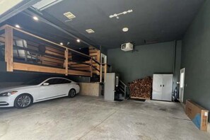 A garage with a white car, wooden shelves, a refrigerator, and a stack of firewood. - Luxury Executive Retreat | Gym & Dual Office (Crystal Lake)