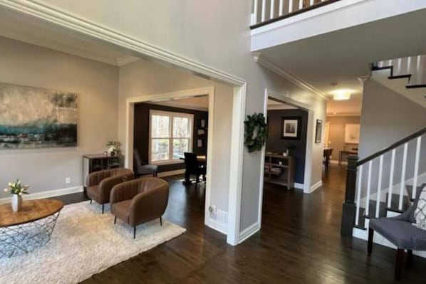 A spacious living room with a fireplace, a dining area, and a staircase leading to an upper level. - Luxury Executive Retreat | Gym & Dual Office (Crystal Lake)