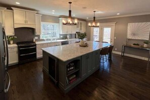 A spacious kitchen with dark wood flooring, white cabinetry, and a large island with bar stools. - Luxury Executive Retreat | Gym & Dual Office (Crystal Lake)