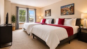 Ein Hotelzimmer mit zwei Betten, einem Fernseher, einem Fenster mit Vorhängen und Bildern an den Wänden.