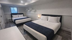 Quarto com duas camas, uma mesinha, uma janela e um criado-mudo.