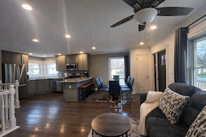 A spacious kitchen with a central island, dining area with chairs, a sofa, and a ceiling fan. - Crystal Lake 4BR | Insurance & Repair Stays (Crystal Lake)