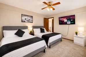 Habitación de hotel con dos camas, ventilador de techo, televisor mostrando servicios de transmisión y puerta que da a otra habitación.