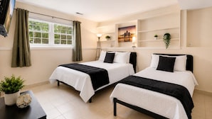 A hotel room with two beds, a TV, a window with curtains, a lamp, and a wall-mounted shelf with plants. - Family Haven in Streamwood | Ideal for Stay Long (Streamwood)