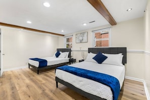 A hotel room with two beds, wooden flooring, a brick wall, and a ceiling with exposed beams. - 5BR Furnished | Insurance Ready | 7 Beds (Rockford)