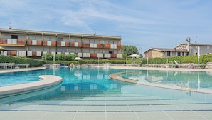 Ein Swimmingpool mit Fliesenveranda, Liegestühlen und einem Gebäude mit Balkonen im Hintergrund.